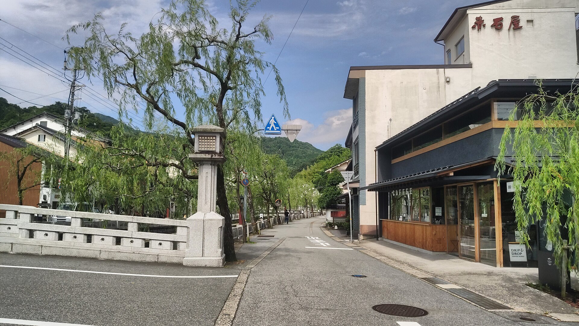 Willow-lined street of Kinosaki Onsen with wooden bathhouses and a stone bridge